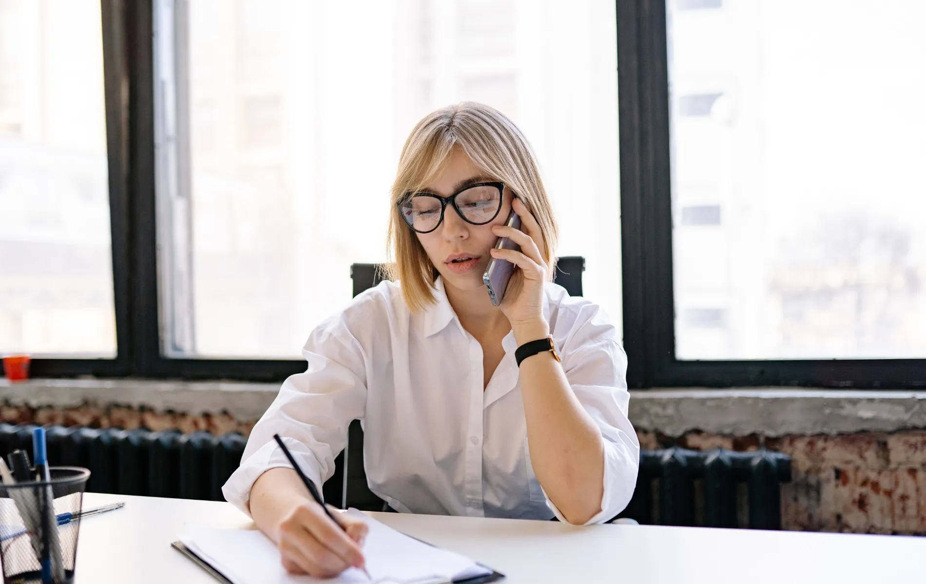Woman taking notes while talking on smartphone