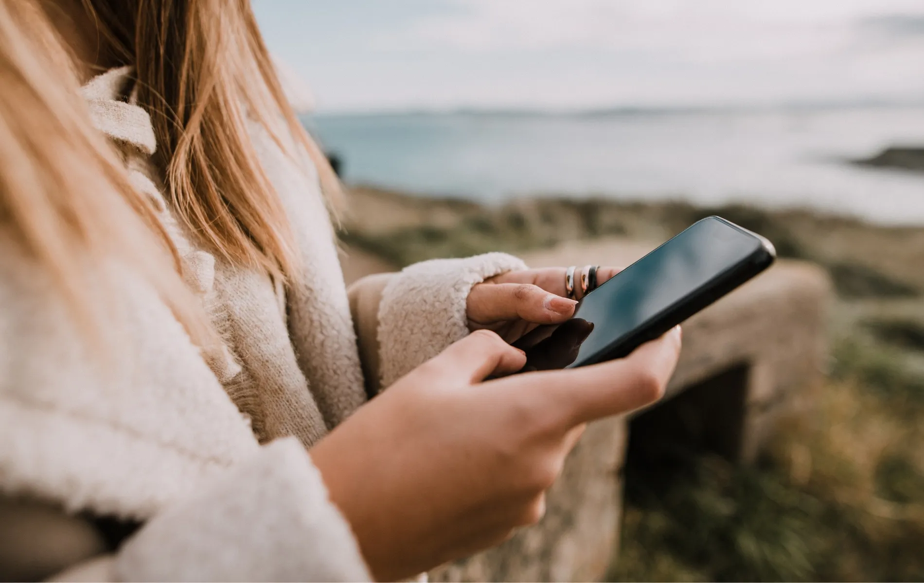 Person using smartphone near coastal overlook.
