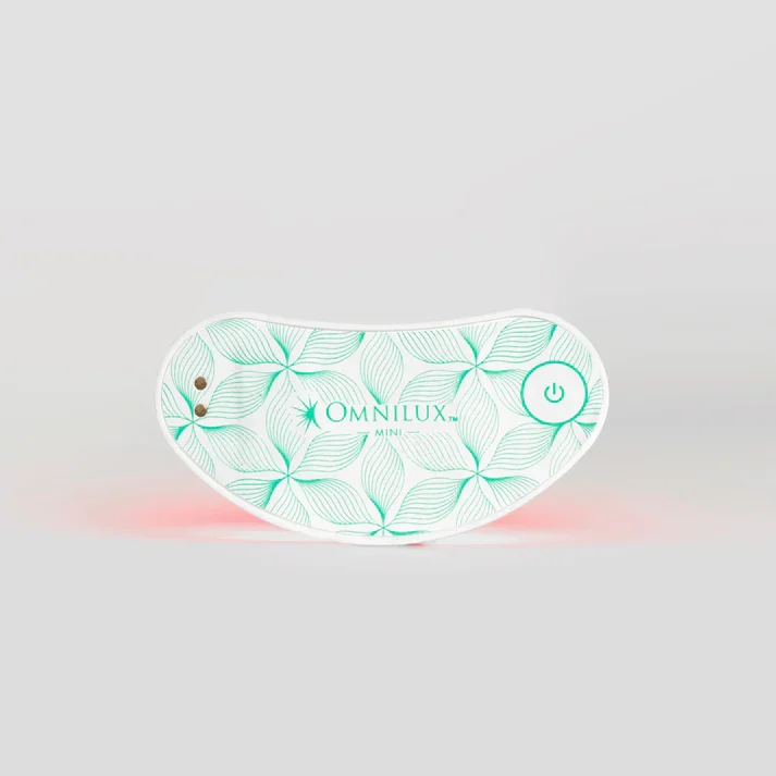 Omnilux Mini LED device featuring a sleek, ergonomic design with a green leaf pattern. The front displays the brand name "Omnilux" and the model "Mini," alongside a power button. This innovative skincare tool is designed for at-home use, utilizing light therapy to enhance skin health and appearance. The soft red light emitted from the device targets signs of aging, promoting collagen production and improving skin texture. Ideal for users seeking a convenient solution for rejuvenating their complexion. The image showcases the device